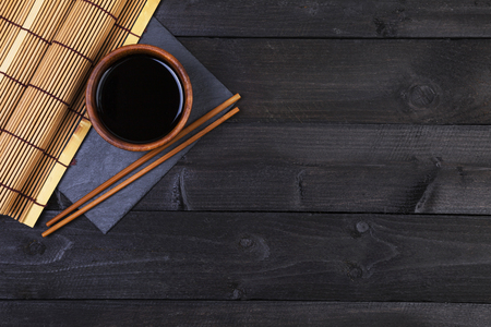 Background for sushi. Bamboo mat, soy sauce, chopsticks on dark table. Top view with copy spaceの写真素材