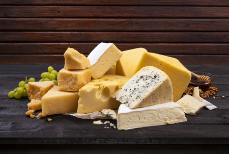 Various types of cheese on black wooden table background. Cheddar, parmesan, emmental, blu cheese. Copy space.の写真素材