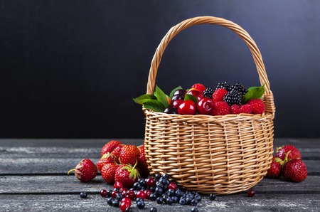 Fresh forest berries in basket on rustic wooden background. Copy spaceの写真素材