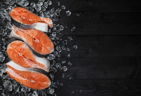 Salmon steak on ice on black wooden table top view, Fish food concept. Copy spaceの写真素材