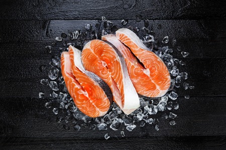 Fresh raw salmon red fish steak on ice on black wooden table top viewの写真素材