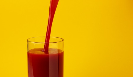 Tomato juice pouring into glass, isolated on yellow color background, with copy spaceの写真素材