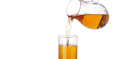 Apple juice pouring from pitcher into glass, isolated on white backgroundの写真素材