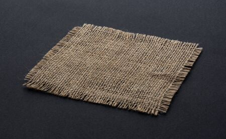 Old burlap fabric napkin closeup. Rough linen jute, sackcloth piece isolated on black background....