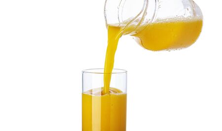 Orange juice pouring from pitcher into glass, isolated on white background, healthy citrus drink with copy spaceの写真素材