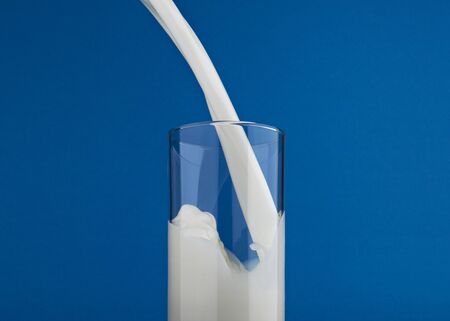 Pouring milk in glass with splash isolated on blue background
