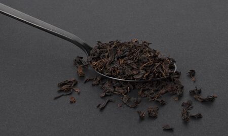 Dry tea leaves in black spoon isolated on black background, creative packaging concept