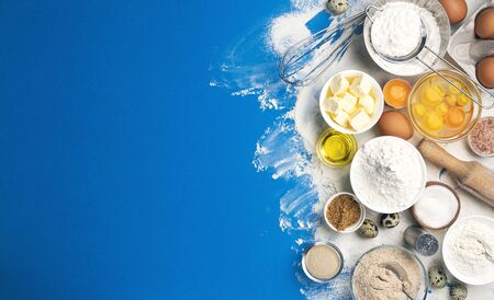 Baking ingredients for dough on blue color background, top view of flour, eggs, butter, sugar and kitchen utensils for homemade baking. Cooking concept banner with copy space for textの写真素材