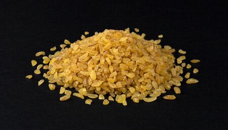Heap of dry bulgur wheat isolated on black background, closeup