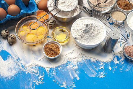 Baking ingredients for dough on blue color background, top view of flour, eggs, butter, sugar and kitchen utensils for homemade baking. Cooking concept banner with copy space for textの写真素材