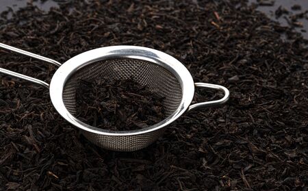 Metal tea strainer with dry black tea leaves, copy space for textの写真素材