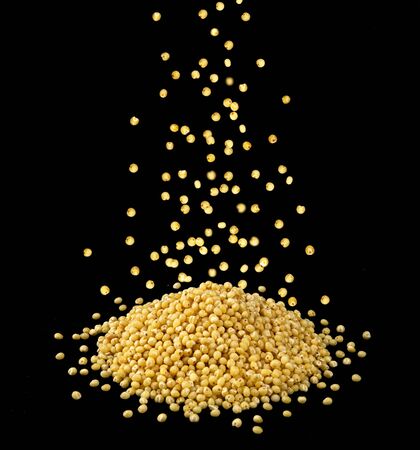 Falling dry millet grains cereal isolated on black background, small heap of millet groatsの写真素材