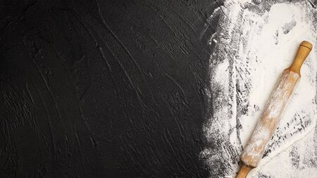 Sprinkled wheat flour and wooden rolling pin on black backgroundの写真素材