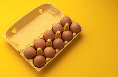 Brown chicken eggs in cardboard box, banner of fresh farm eggs on yellow background, top view with copy space for textの写真素材