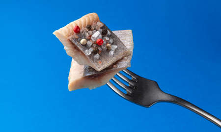 Pieces of salted herring on fork isolated on blue background, slices of smoked marinated mackerel...
