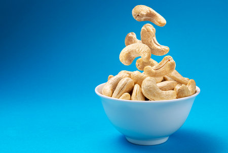 Falling cashew nuts into bowl on blue backgroundの写真素材