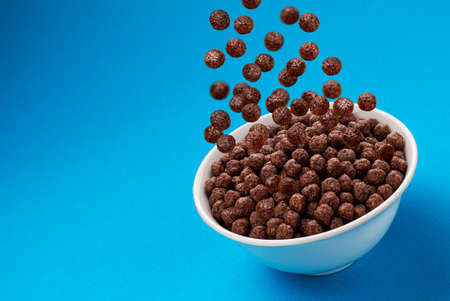 Chocolate Corn balls falling in bowl over blue background