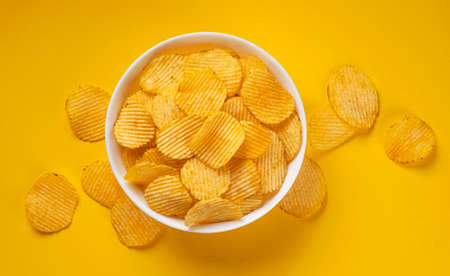Ridged potato chips in bowl on yellow backgroundの写真素材