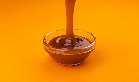 Pouring caramel sauce in glass bowl on color backgroundの写真素材
