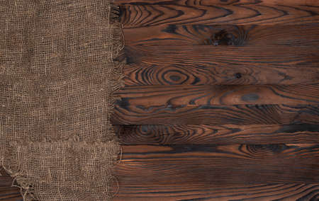 Old burlap fabric napkin on brown wooden background, top view. Rough linen jute, sackcloth piece on dark wooden table. top viewの写真素材