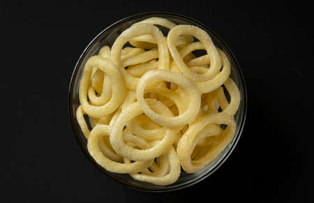 Crispy onion rings in bowl on black background, top view