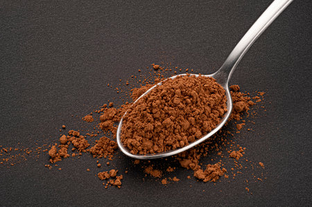 Cocoa powder in spoon on black background