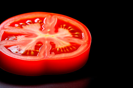 Tomato slice over black background with copy spaceの素材