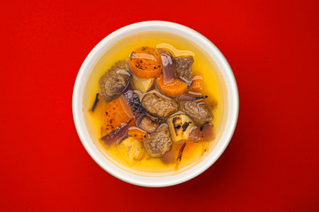 Beef stew with broth, soup with meat and vegetables on red backgroundの写真素材
