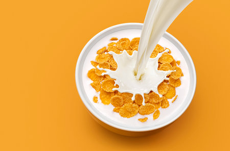 Bowl of corn flakes breakfast with pouring milk and splash isolated on yellow background with copy...