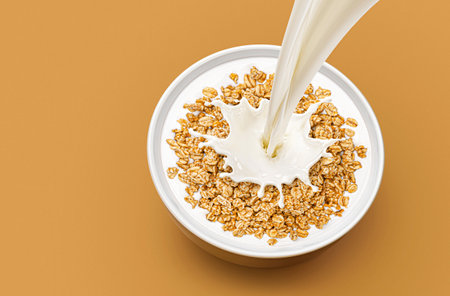 Bowl of granola breakfast with pouring milk and splash isolated on light beige background with copy...