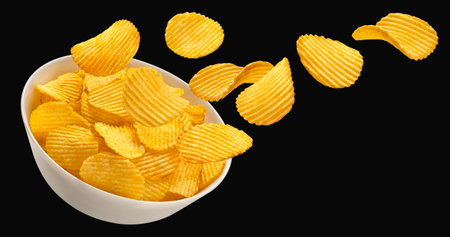 Falling ridged potato chips in bowl isolated on black background, package design elementの写真素材