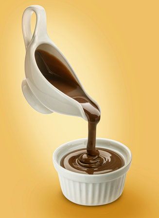 Chocolate cream pouring from ceramic creamer into white bowl on yellow backgroundの写真素材