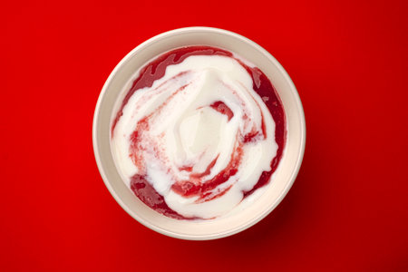 Bowl of yogurt with berry jam swirl on red background with copy space, top viewの写真素材