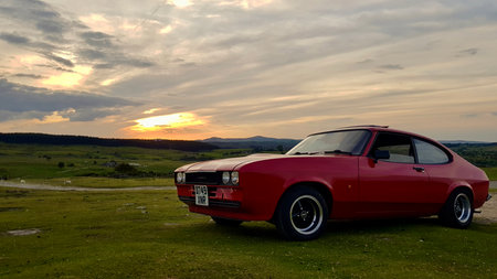 Old car at sunset in a field with mountains in the backgroundの写真素材