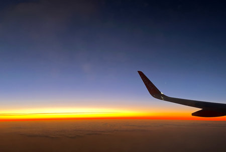 Wing of an airplane flying above the clouds at sunset in the eveningの写真素材