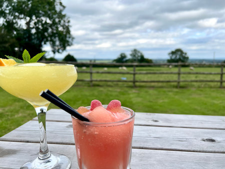 Two cocktails on a wooden table in front of a countryside landscape.の写真素材