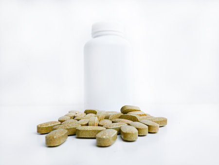 Pills spilling out of pill bottle on white background. Focus on foreground.の写真素材