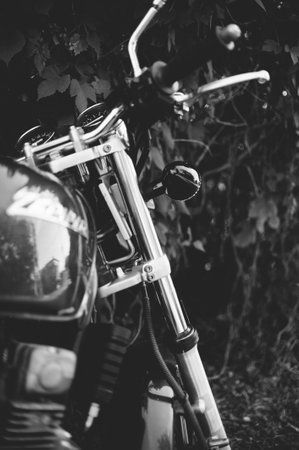 A close-up, black and white photograph of a motorcycle's front end, featuring the headlight,...