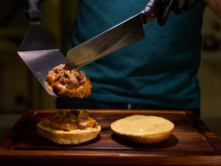 A man is preparing a sandwich with a spatula. The sandwich is topped with meat and onionsの写真素材