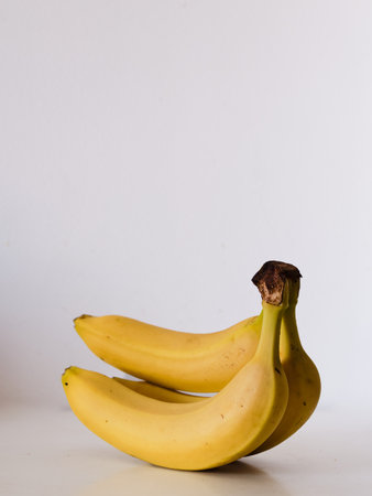 Three bananas are sitting on a white table. The bananas are yellow and appear to be ripe. Concept of freshness and abundance, as the bananas are a healthy and nutritious snack optionの写真素材