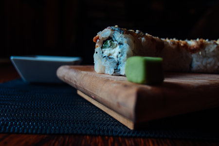 A sushi roll with a piece of avocado on top sits on a wooden cutting board. The roll is cut in half and placed on a black clothの写真素材