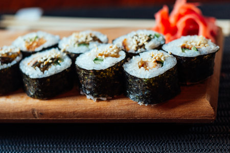 A plate of sushi with a garnish of red ginger. The sushi is arranged in a neat row on a wooden boardの写真素材