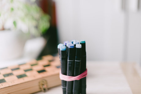 A box of pens is on a table next to a chess board. The pens are black and blueの写真素材