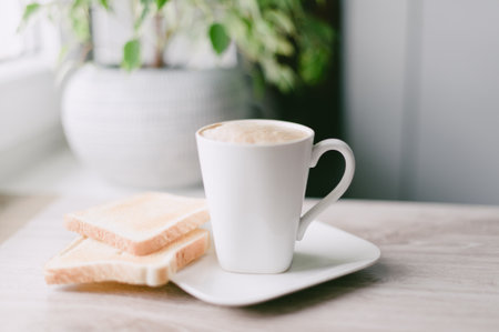 A white coffee cup with a white plate of toast. The toast is cut in half and placed on the plateの写真素材