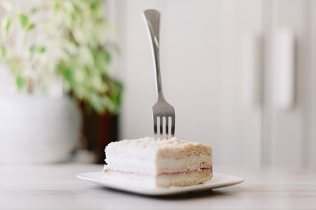 A fork is sticking out of a piece of cake on a white plate. The fork is bent at the top and the cake is cut into a squareの写真素材