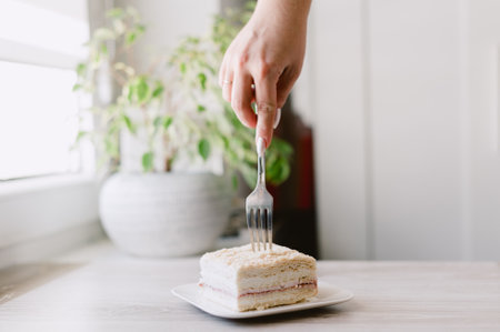 A person is cutting a piece of cake with a fork. The cake is on a white plate
