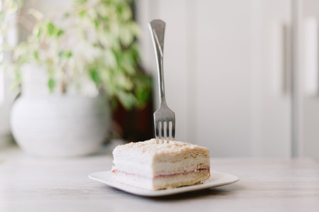A fork is sticking out of a piece of cake on a white plate. The fork is bent at the top and the cake is cut into a squareの写真素材
