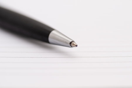 A pen is sitting on a spiral bound notebook. The pen is black and has a silver tipの写真素材