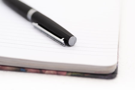 A pen is on a white page of a notebook. The pen is black and has a silver tipの写真素材