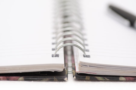 A spiral bound notebook with a pen on top of it. The notebook is open to the middle of the pageの写真素材
